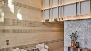 A lobby with a high ceiling, a marble fireplace, and two armchairs. - Amaya (Broadbeach)