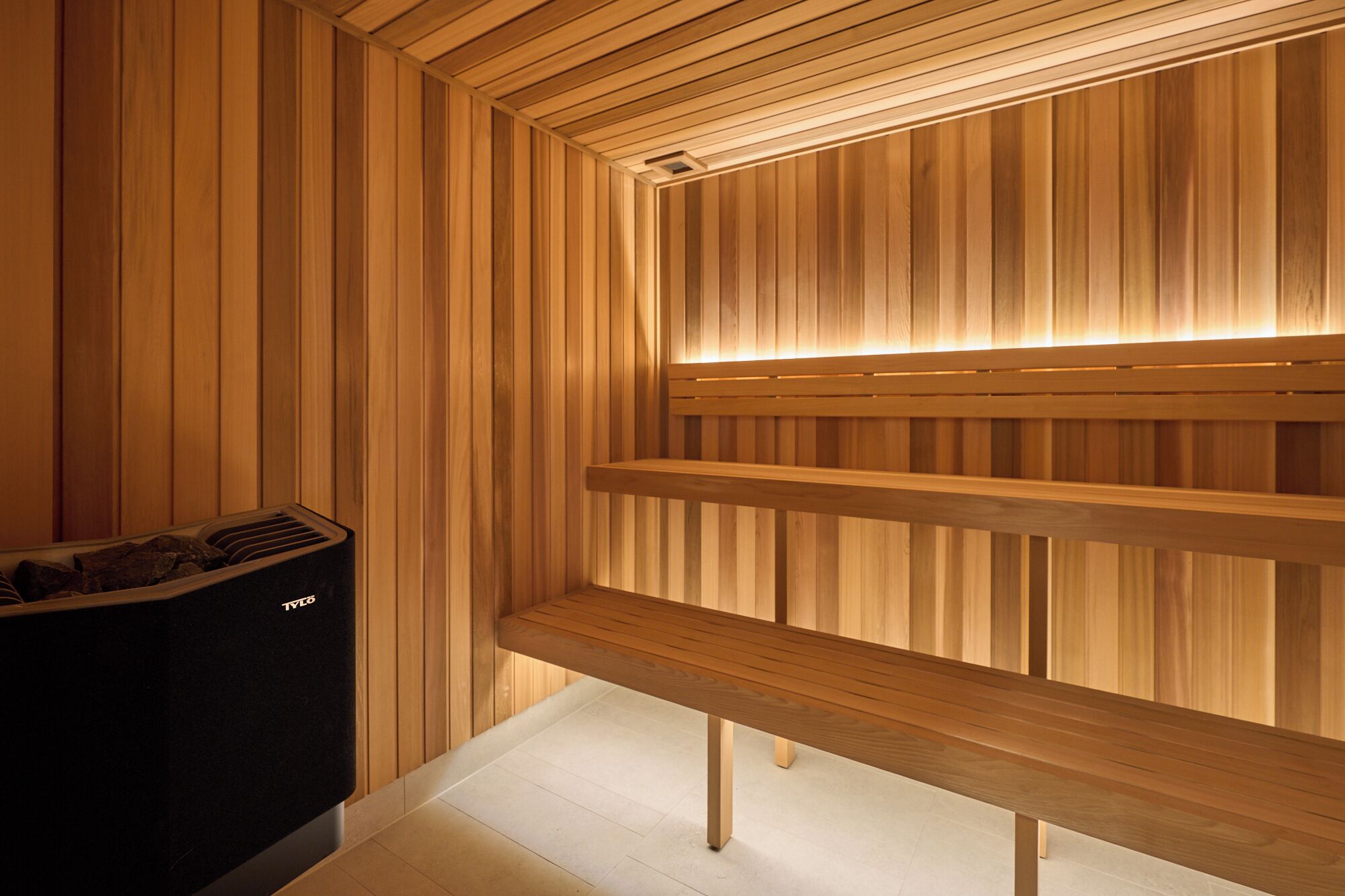 A sauna with wooden benches and a black heater.