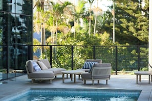 A poolside area with a sofa, chairs, and a small table. - Amaya (Broadbeach)