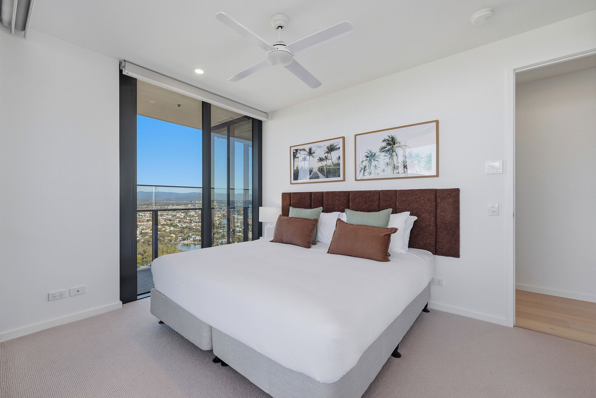 Quarto com uma cama grande, um ventilador de teto e vista para a cidade através de uma janela ampla.