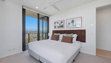Quarto com uma cama grande, um ventilador de teto e vista para a cidade através de uma janela ampla.