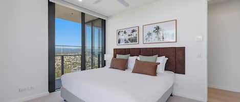 A bedroom with a large bed, a ceiling fan, and a view of a cityscape through a large window.