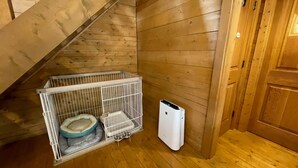 Quarto de canto com paredes de madeira, caixa de transporte para animais, cama para animais e aquecedor branco.