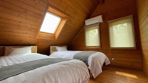 Um quarto de sótão acolhedor, com duas camas, paredes de madeira, um claraboia e uma janela com persianas.