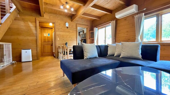 A wooden cabin interior with a sofa, a table, and a small white appliance.