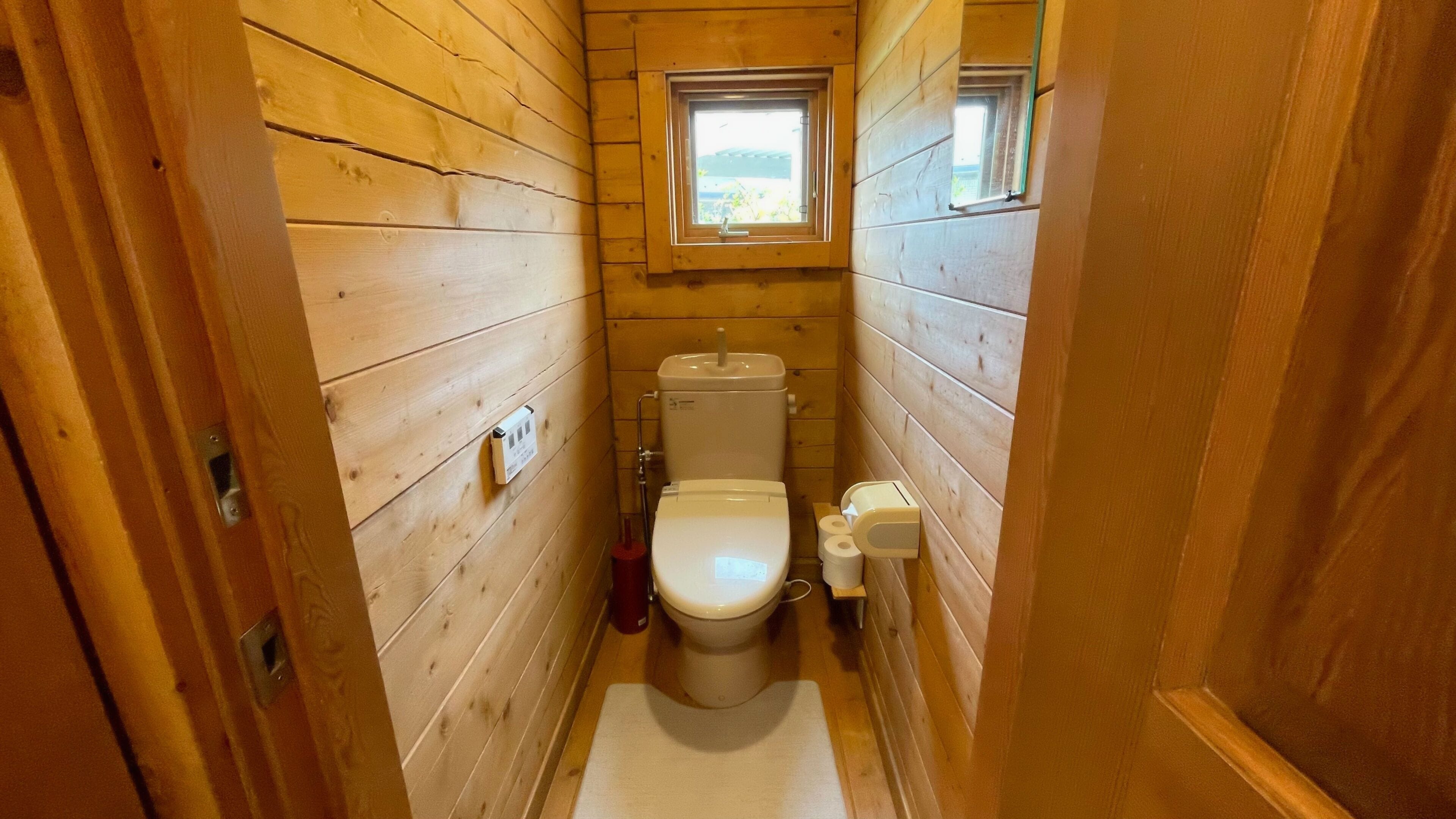 Un baño de madera estrecho con un inodoro, un ventanal pequeño y un dispensador de toallas.