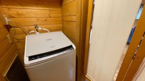 Máquina de lavar compacta e branca num quarto de madeira, com uma porta que dá para outro espaço.