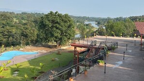 Un área de piscina con vista a un río y árboles, un paseo techado y un patio con plantas en macetas.
