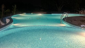 Una piscina nocturna con agua cristalina, una luna en el cielo y un árbol al fondo.