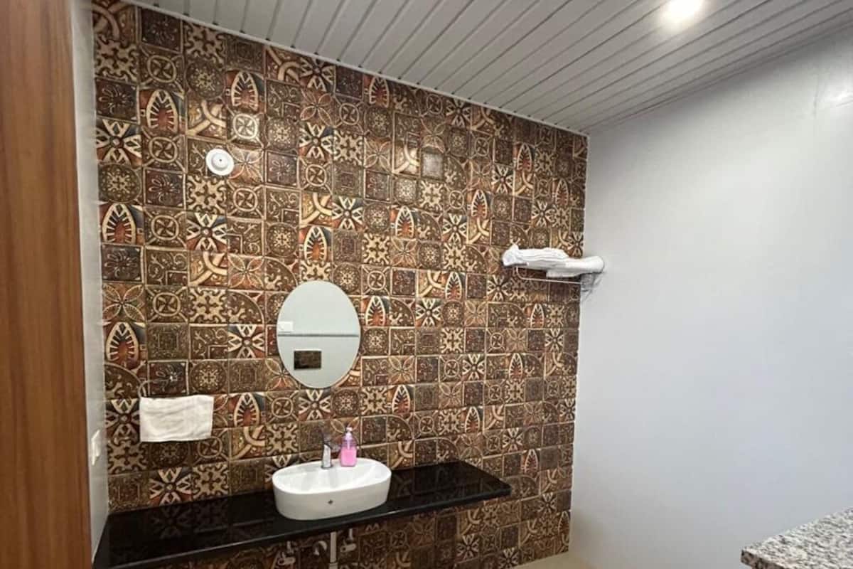 Un baño con pared de azulejos estampados, un espejo redondo, un lavabo con encimera negra y un inodoro.