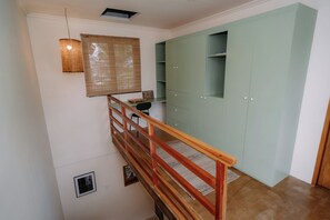 Una escala amb barana de fusta, un penjall decoratiu de fibra i un moble d'emmagatzematge verd amb prestatgeries.
