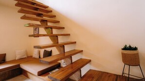 Una escalera de madera con asientos integrados, una planta en un pedestal y un cuadro en la pared.