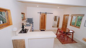 Una cocina moderna con una isla central, un comedor con una mesa y sillas de madera, y una puerta corrediza que da a otra habitación.