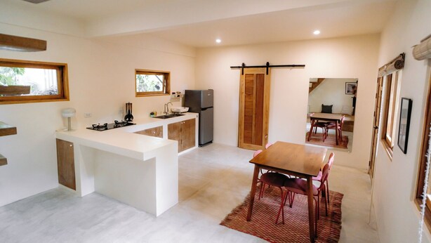 Cocina compacta con una isla central, zona de comedor con mesa de madera y puerta corrediza que da a una sala de estar.