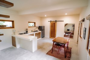 Cuina compacta amb una illa central, zona de dinar amb taula de fusta, i una porta corredissa que dóna a un espai saló.