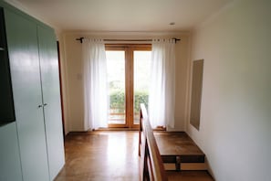 Una habitación con un banco de madera, una puerta corredera con cortinas y vistas al verdor exterior.