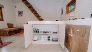 Una cocina con alacenas abiertas que exhiben utensilios, un banco de madera y una escalera.