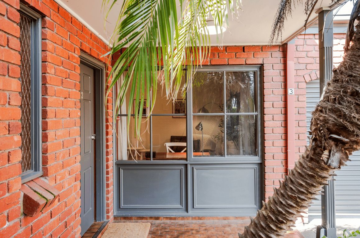 Un edificio de ladrillo con un gran ventanal, una puerta y una palmera.