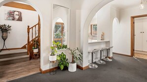 A hallway with white walls, wooden flooring, and a staircase. There are potted plants, a mirror, and a door. - Belle Escapes - Glenelg Urban Escape (Holdfast Bay)