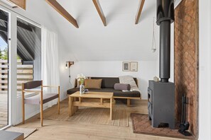 Ein Wohnzimmer mit einer Couch, einem Holztisch, einem Sessel, einem Kamin und Blick durch eine Schiebetür.