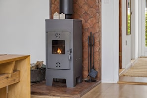 Ein Kaminofen mit Feuer, eine Steinsäule und ein Holztisch.