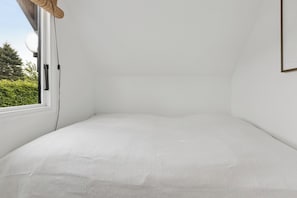 Ein Zimmer mit einem weißen Bett, einem Fenster und einer Tür.