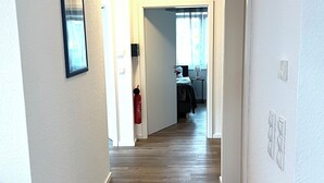 Ein Flur mit Holzboden, weißen Wänden und einer Tür zu einem Zimmer mit Bett und Fenster.