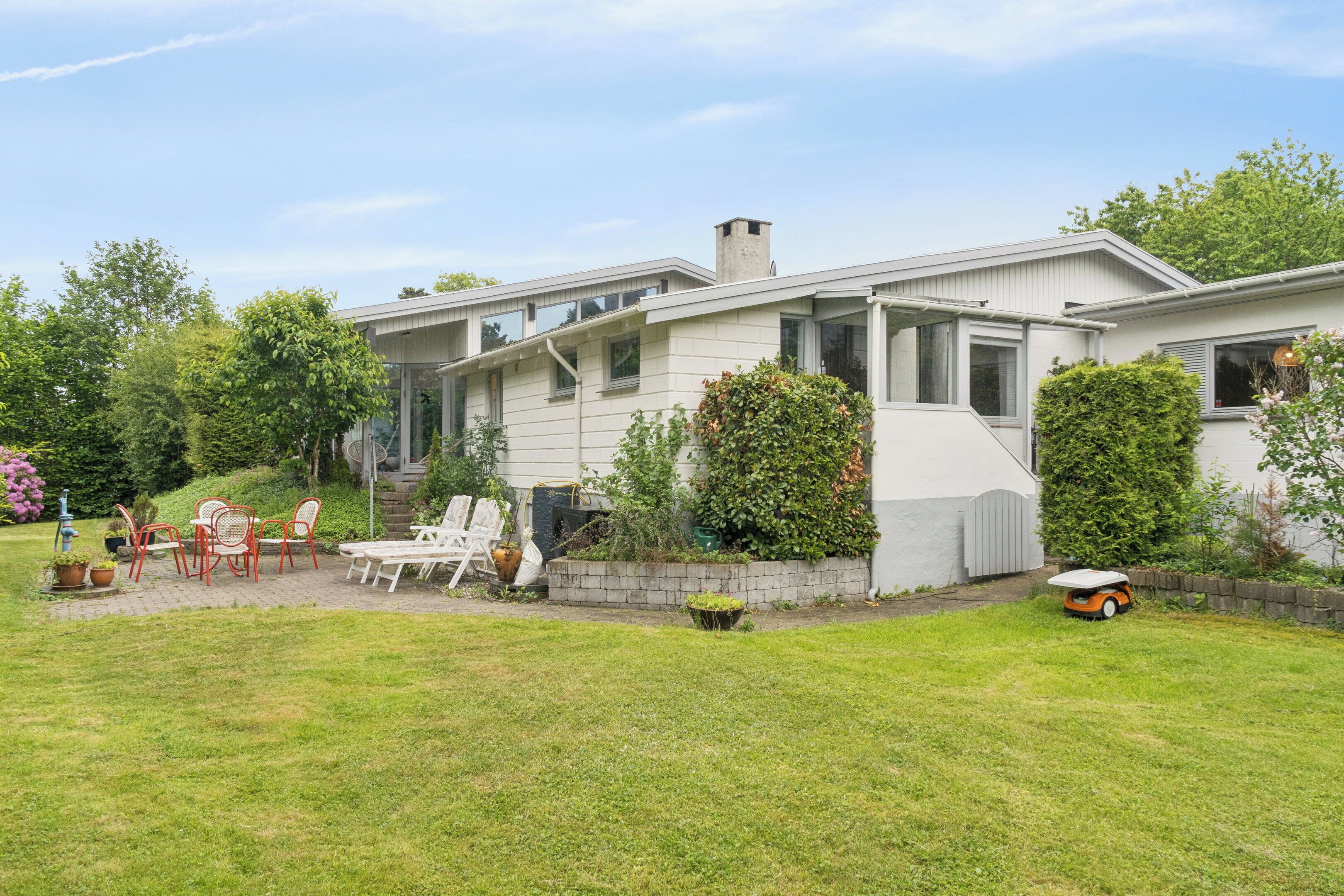 Uma casa moderna com um pátio, móveis de exterior e um gramado bem cuidado.