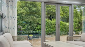 A modern outdoor patio with a sofa, table, and large glass doors leading to a garden.