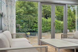 Eine moderne Außenpatio mit einer Couch, einem Tisch und großen Glasfenstern zum Garten hin.