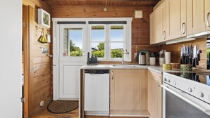 Une cuisine compacte aux murs en bois, équipée d’un lave-vaisselle, d’une cuisinière et d’une fenêtre donnant sur un espace verdoyant.