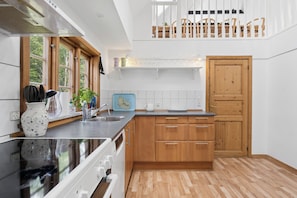 A kitchen with wooden cabinets, a black countertop, and a view of the outdoors through large windows. - Lovely holiday home by the Baltic Sea (Gudhjem)