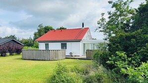 A white house with a red roof, surrounded by a well-maintained lawn and dense greenery.
