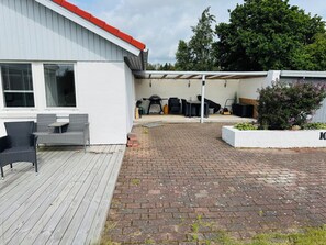 A covered patio with outdoor furniture, a barbecue grill, and a white building with a red roof. - Cozy holiday home in beautiful nature (Hadsund)