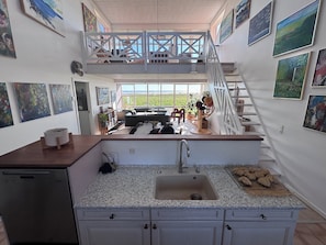 A kitchen with a sink, countertop, and cabinets. There is a staircase leading to a balcony with a view.