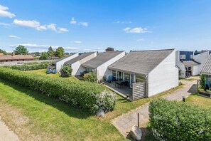 Eine Reihe moderner, weißer Häuser mit geneigten Dächern, ein gepflegter Garten und ein klarer, blauer Himmel.