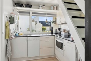 Eine moderne Küche mit weißen Schränken, einem Geschirrspüler, einem Backofen und einem Fenster mit Blick auf eine Wohngegend.