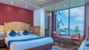 A hotel room with a wooden headboard bed, a dining table with chairs, and a large window offering a view of the outdoors. - The Wood Inn (Shimla)