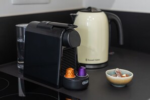 Een keuken met een koffiezetapparaat, een waterkoker en een kom met noten op een zwart aanrecht.