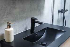 Een moderne badkamer met een zwart wastafel, een zeepdispenser en een douchegedeelte.