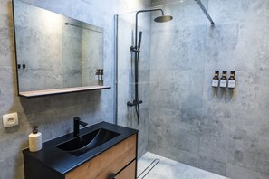 Een moderne badkamer met een zwart wastafel, een spiegel, een douche en drie flessen shampoo aan de muur.
