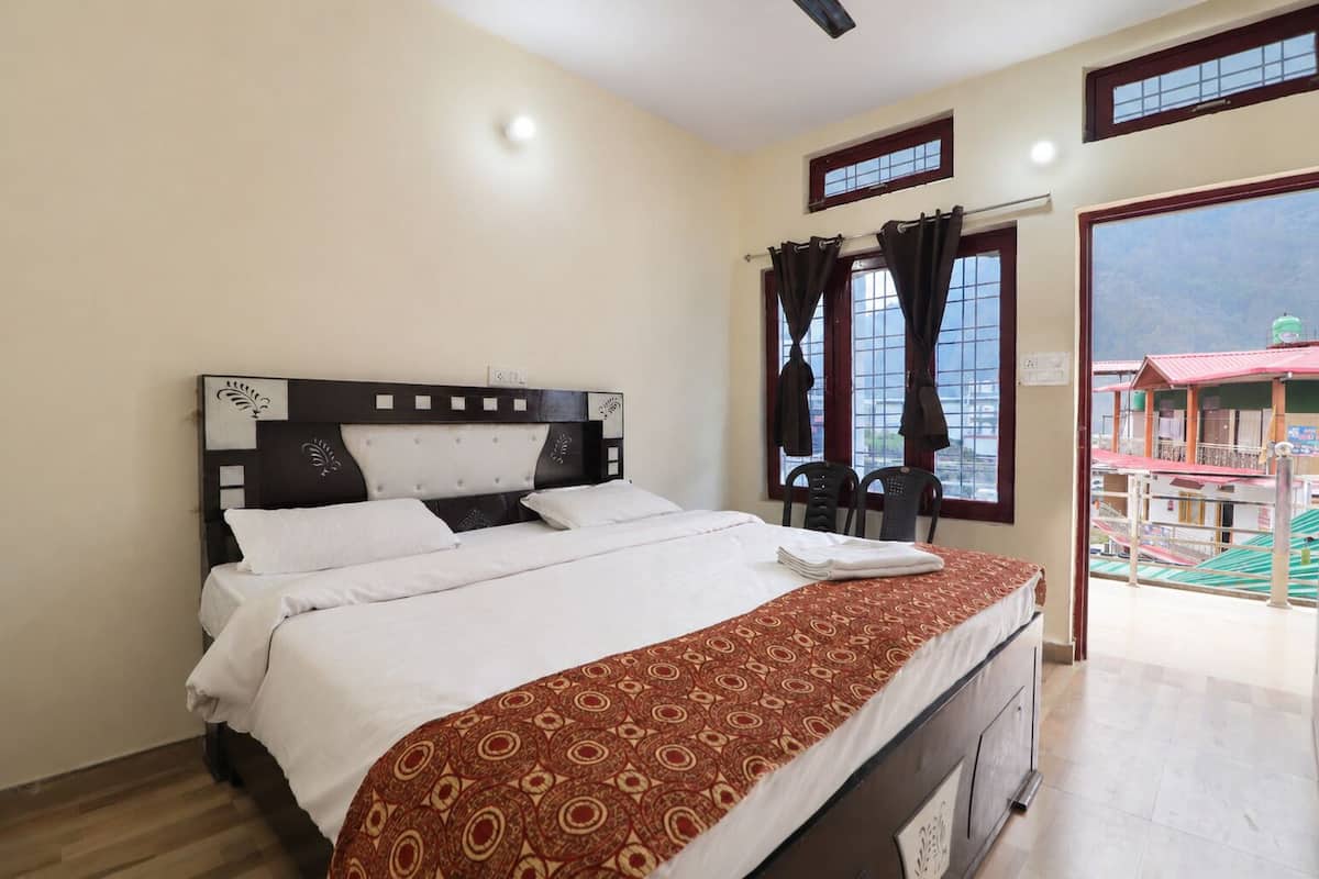 A bedroom with a bed, a window with curtains, a view of buildings outside, and a door leading to a balcony.