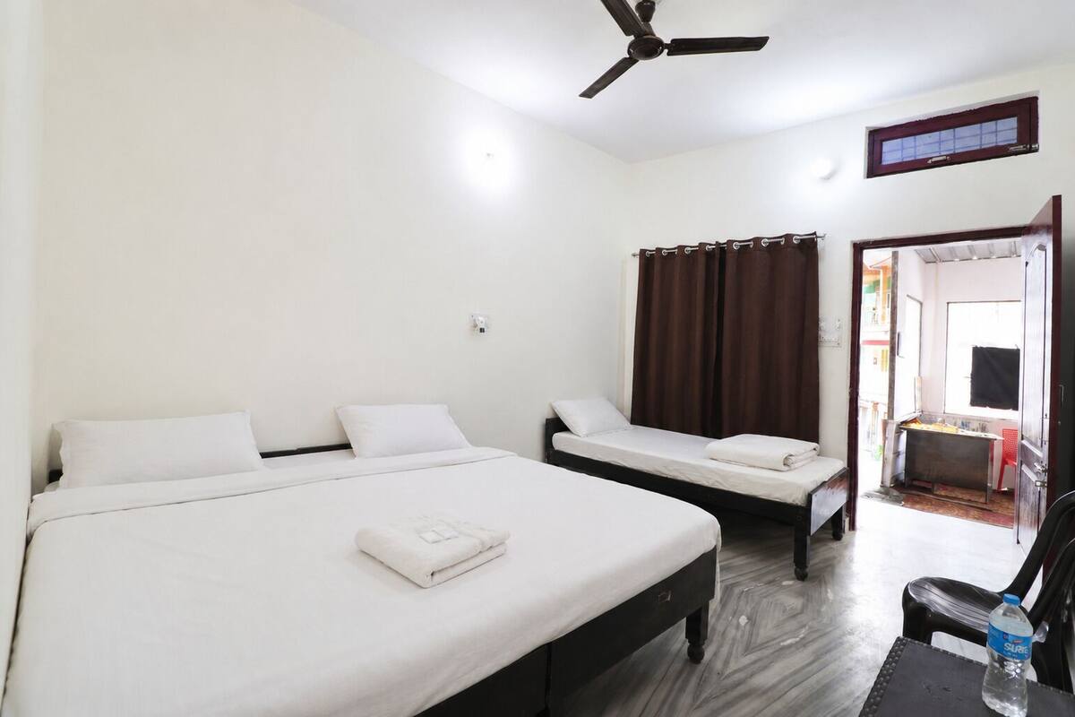 A hotel room with two beds, a ceiling fan, a window with curtains, and a door leading to a balcony.
