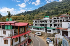 Un hotel con un edificio de techo rojo, un edificio blanco con múltiples ventanas y un telón de fondo montañoso.