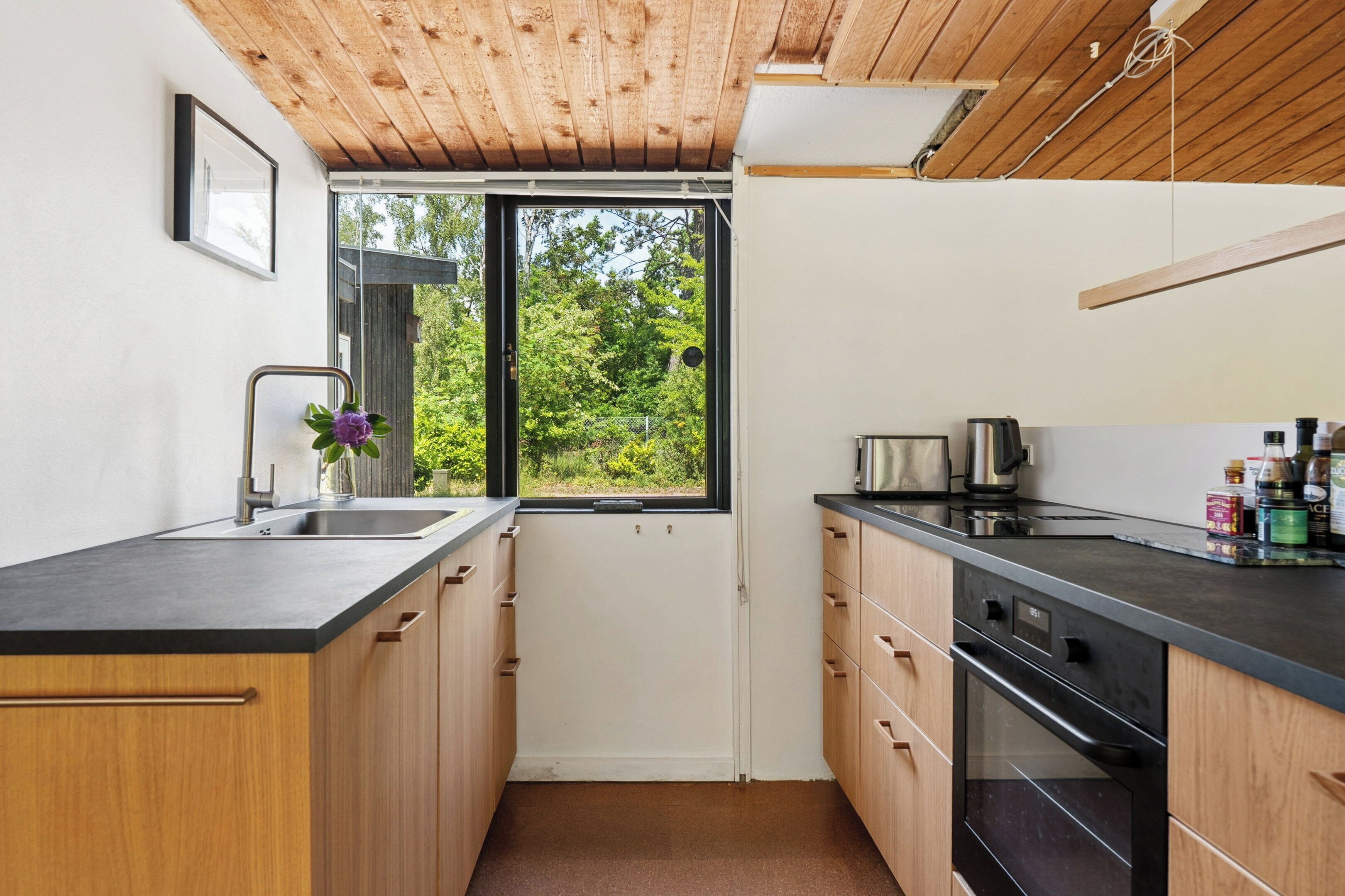 Een moderne keuken met houten kastjes, een zwart aanrecht en een raam met uitzicht op groen.