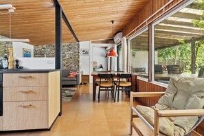 Eine moderne Küche mit Holzschränken, einem Essbereich mit Stühlen und einem großen Fenster mit Blick ins Freie.