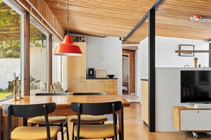 Eine moderne Küche mit Holzschränken, einem Esstisch mit Stühlen, einer roten Pendelleuchte und einem Fernseher auf einem Schrank.