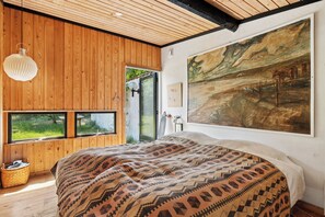 Ein Schlafzimmer mit einem großen Bett, Holzwänden, einem Gemälde und Blick durch ein Fenster.