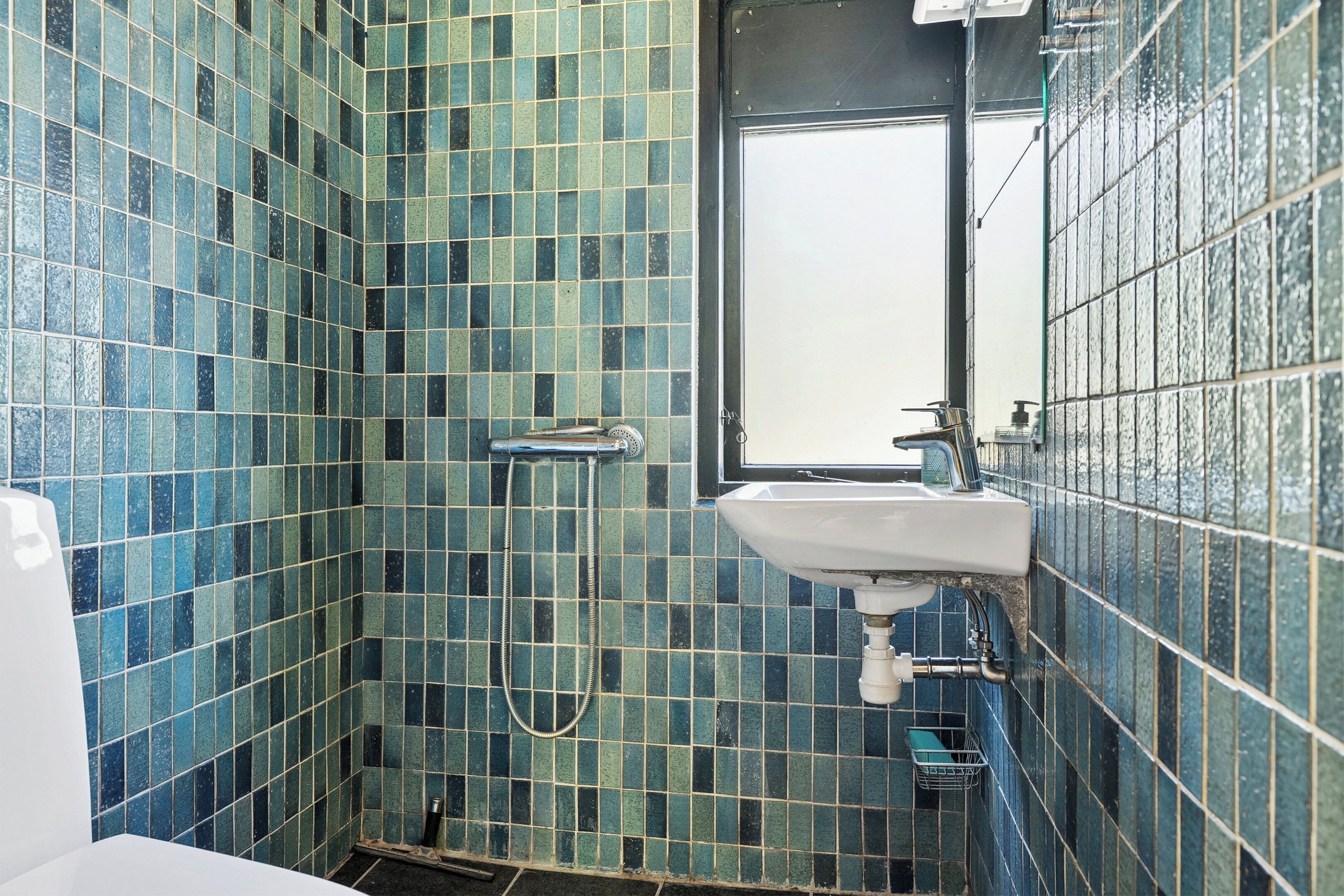 A bathroom with blue-tiled walls, a white sink, and a handheld showerhead.