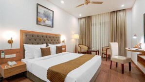 Quarto de hotel com uma cama grande, uma escrivaninha, uma cadeira, um ventilador de teto e um quadro na parede.